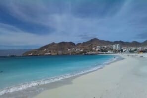 a beach with blue water and mountains in the background