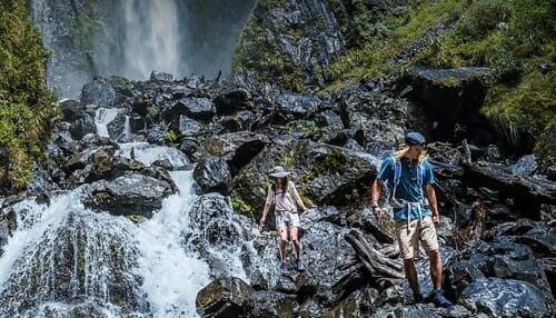 a group of people walking on rocks near a waterfall