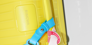 RIMOWA x CHAOS Limited Edition Adds a Drop of Colour to the Iconic Cabin Case a yellow suitcase with a blue tag attached to it