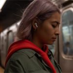 Best Travel Tech Deals: Apple AirPods Pro £40 Off (UK) a woman with purple hair wearing a white earbud and red hoodie