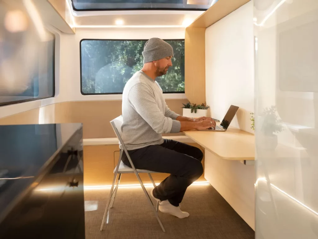 a man sitting at a desk with a laptop.  CES 2024 News Pebble Flow Electric RV.  {Tech} for Travel. https://techfortravel.co.uk