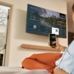 a woman sitting on a bed looking at a television screen. IHG AirPlay