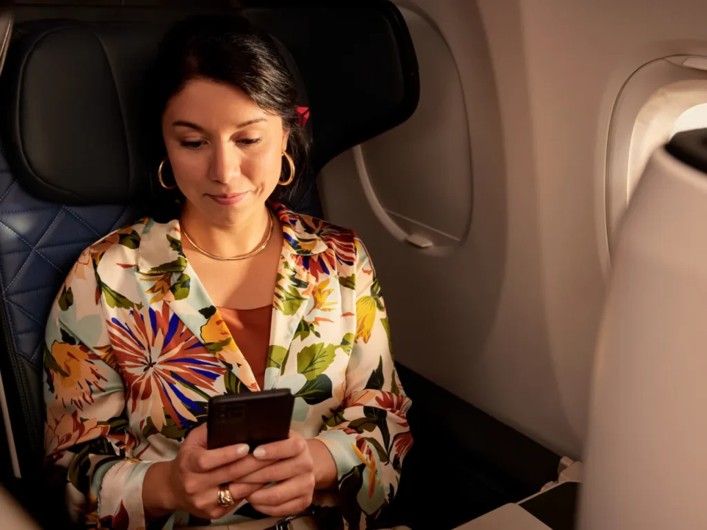 a woman sitting in an airplane looking at a cell phone. Fly Delta App.  {Tech} for Travel. https://techfortravel.co.uk