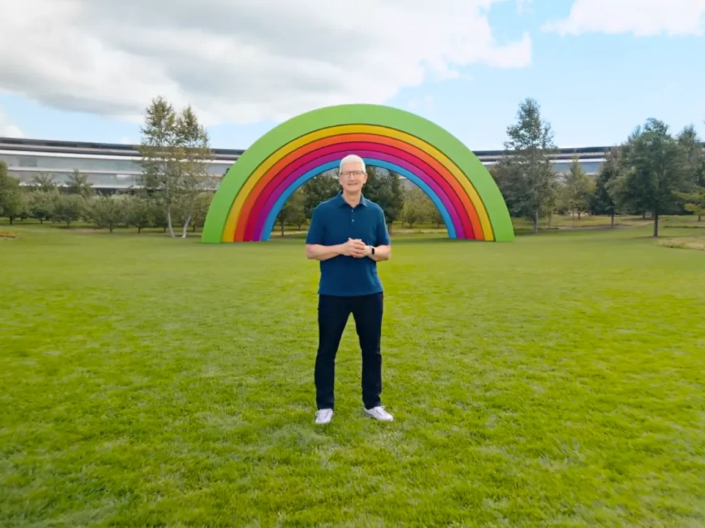 a man standing in a grassy field with a rainbow in the background. Tim Cook launches Apple iPhone 16.  {Tech} for Travel. https://techfortravel.co.uk