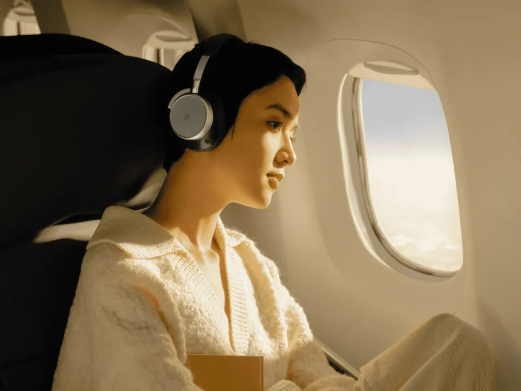 a woman wearing headphones and looking out of an airplane window. B&O Beoplay H100 Headphones.  {Tech} for Travel. https://techfortravel.co.uk