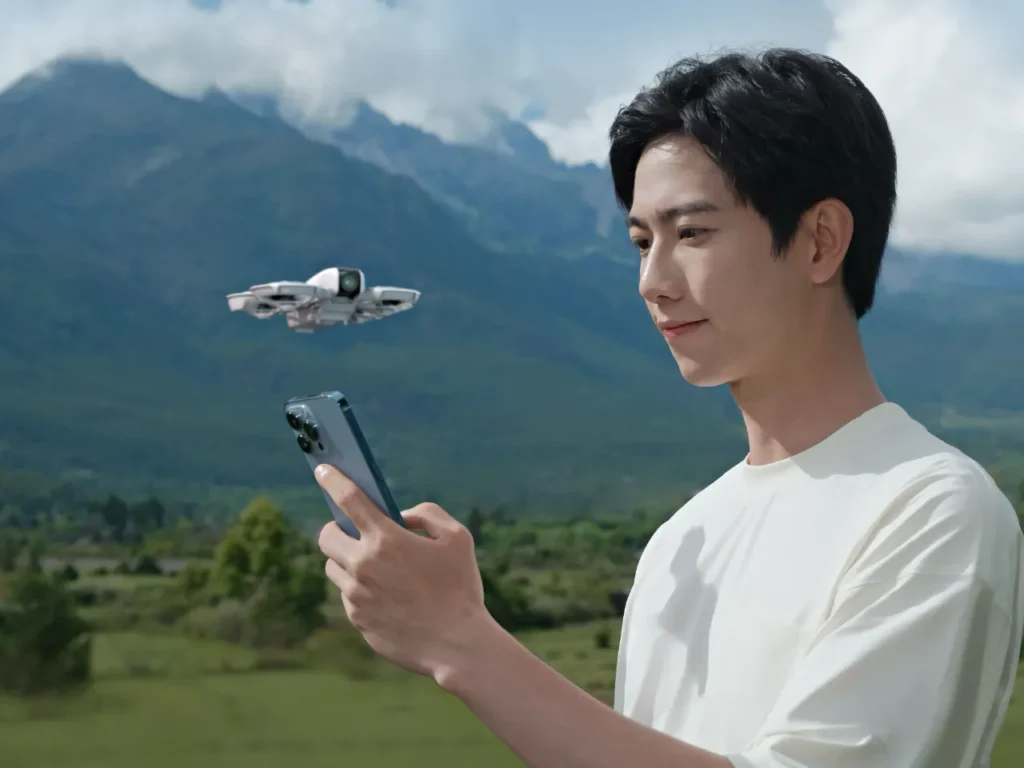 a man holding a phone and looking at a flying drone. DJI Neo