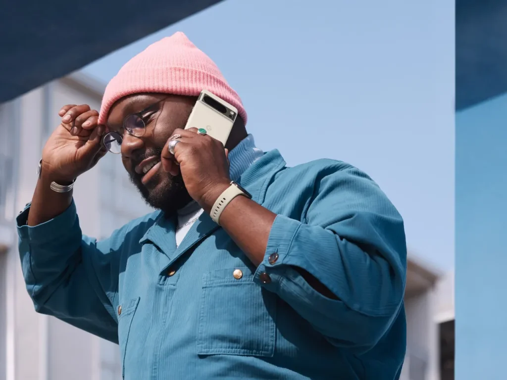 a man in a blue shirt and pink hat talking on a cell phone.  Google Pixel 8 Pro. Best Travel gadgets 2024. {Tech} for Travel. https://techfortravel.co.uk