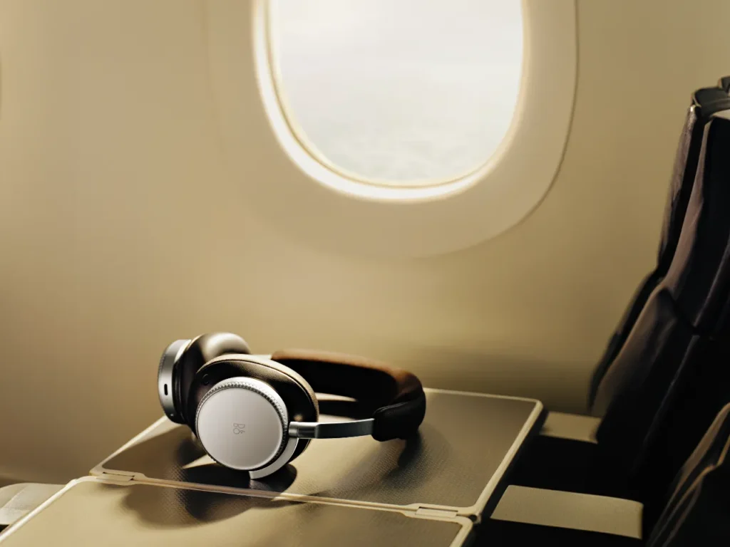 headphones on a table in an airplane. B&O Beoplay H100. Best Headphones for Travel 2025.  {Tech} for Travel. https://techfortravel.co.uk