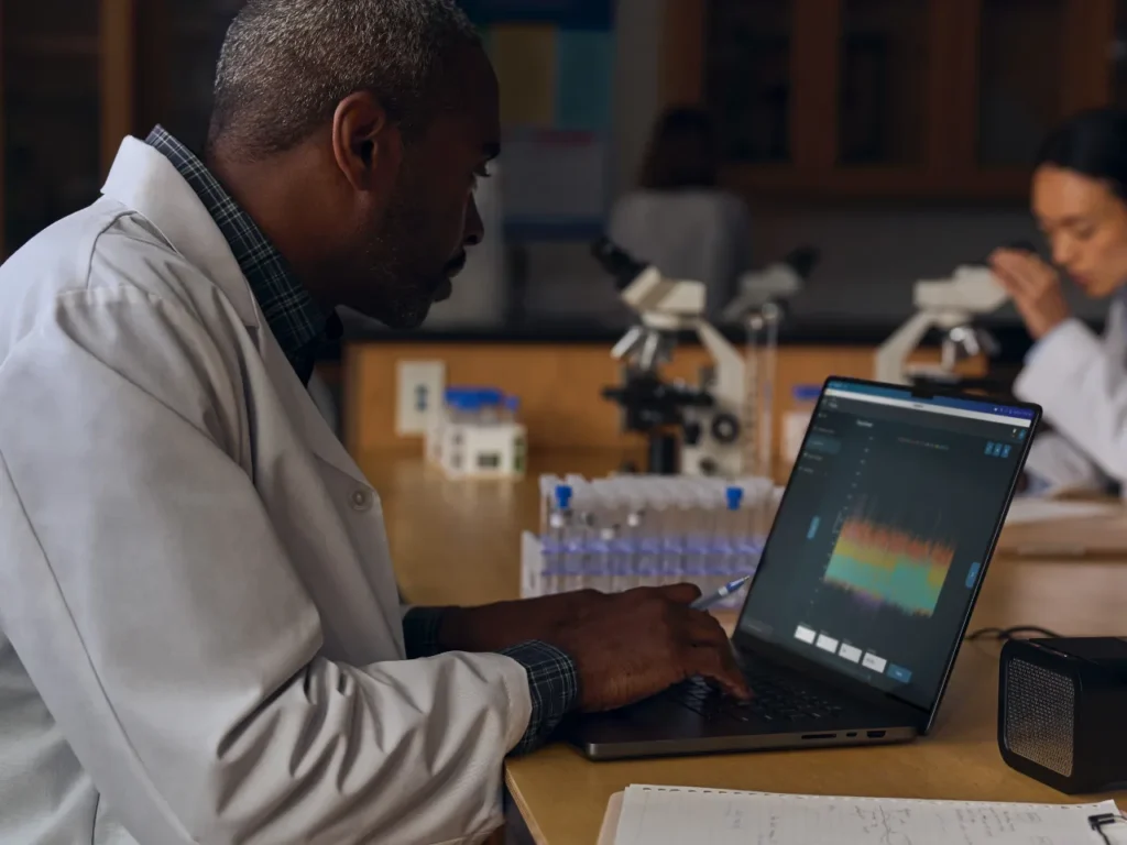 a man in a lab coat working on a laptop. Apple MacBook Pro M4 Specifications.  {Tech} for Travel. https://techfortravel.co.uk