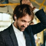 CES 2025 News: OpenRock X A New Era in Open Ear Design a man with a beard wearing a white shirt and black jacket. OpenRock X headphones. {Tech} for Travel. https://techfortravel.co.uk