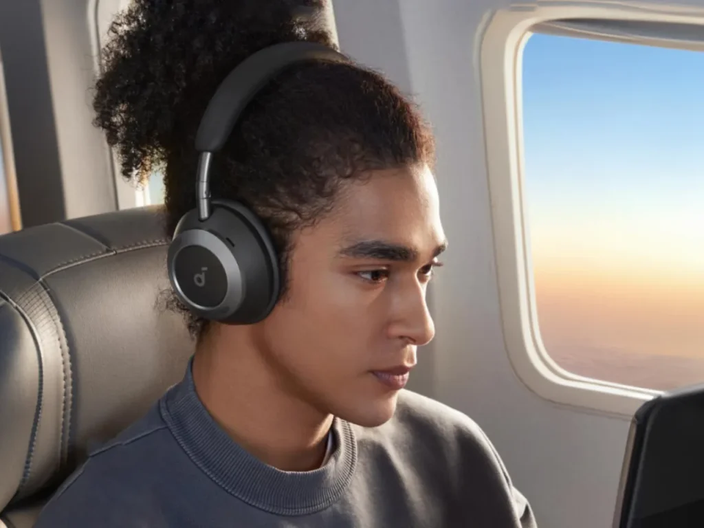 a person wearing headphones looking out of a window. Best Headphones for Travel 2025.  {Tech} for Travel. https://techfortravel.co.uk