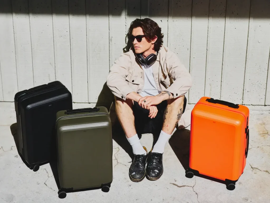 a man sitting on the ground with his luggage. Aer Carry-On Max. Best Carry-On Cases 2025. {Tech} for Travel. https://techfortravel.co.uk