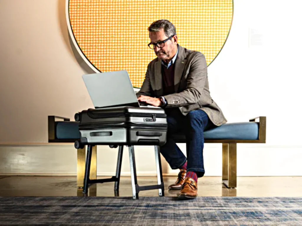 a man sitting on a bench using a laptop. PROPS Luggage Carry on.  Best Carry On Cases 2025. {Tech} for Travel. https://techfortravel.co.uk