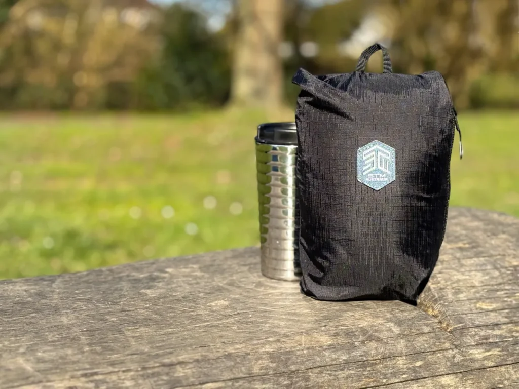 a black bag and a metal mug on a wood bench. STM Goods BagPack review. {Tech} for Travel. https://techfortravel.co.uk