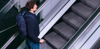 New Carl Friedrik x Williams F1 Luggage Collection Launches a man with a backpack and luggage on an escalator. Carl Friedrik x Williams F1 Luggage Collection. {Tech} for Travel. https://techfortravel.co.uk