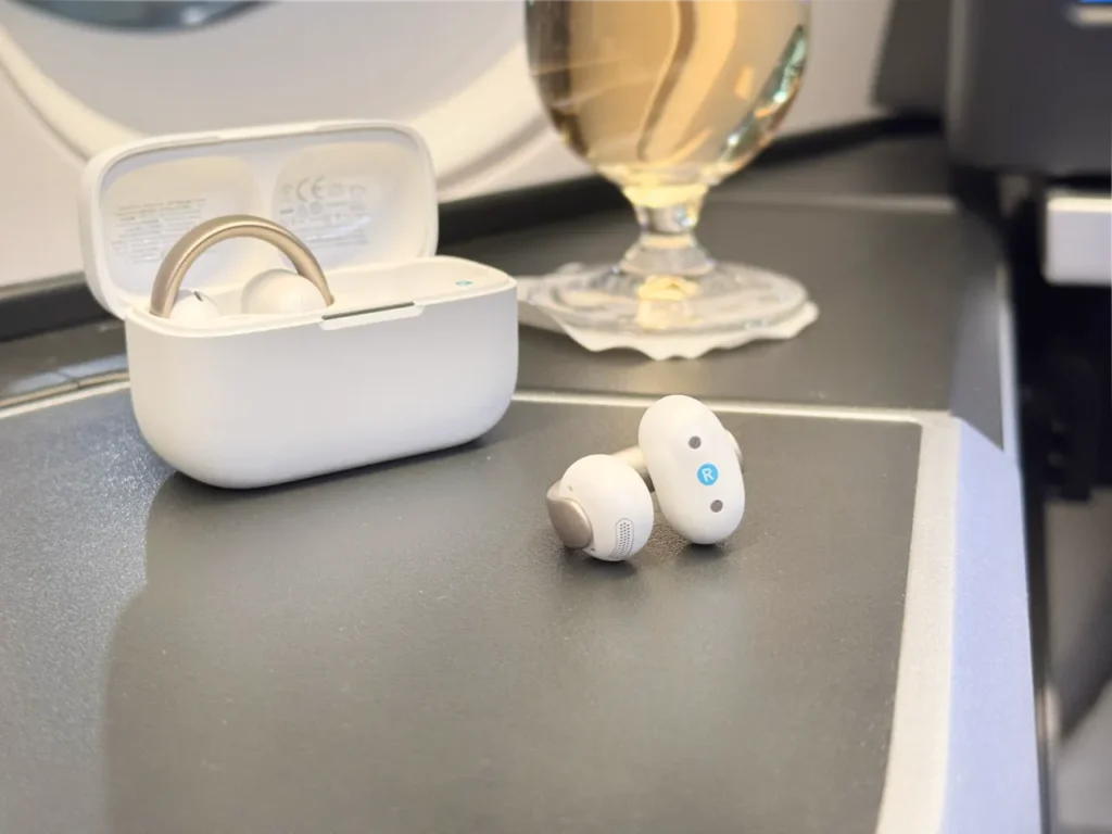 a pair of white earbuds next to a glass of liquid. Soundcore Aeroclip review. {Tech} for Travel. https://techfortravel.co.uk