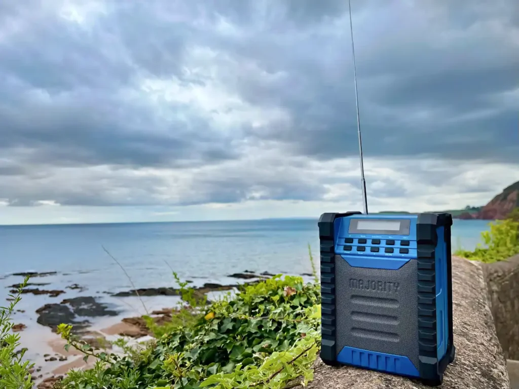 Majority Lanbeach speaker front – {Tech} for Travel a blue radio on a rock by the ocean. Majority Landbeach speaker review. {Tech} for Travel. https://techfortravel.co.uk