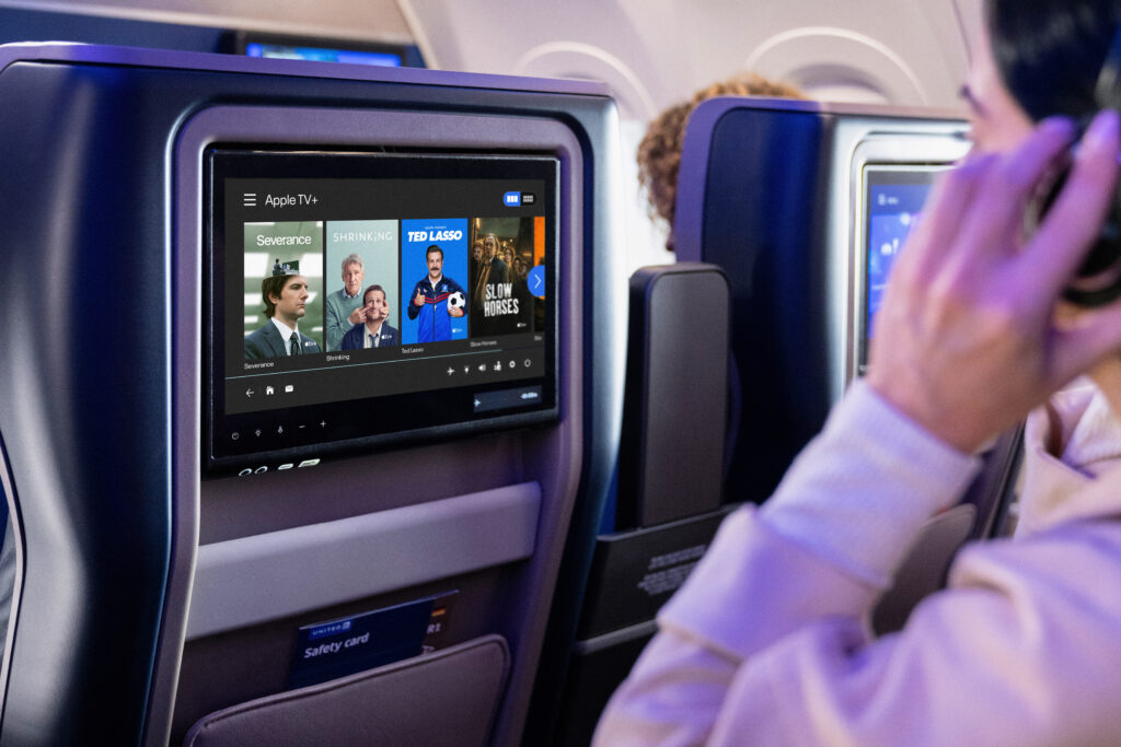 United x AppleTV+ – {Tech} for Travel a man sitting in an airplane with a television screen. United Airlines Apple TV+. {Tech} for Travel. https://techfortravel.co.uk