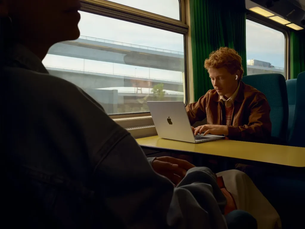 a man sitting at a table with a laptop. Apple AirPods Pro 3. {Tech} for Travel. https://techfortravel.co.uk