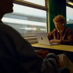 a man sitting at a table with a laptop. Apple AirPods Pro 3. {Tech} for Travel. https://techfortravel.co.uk