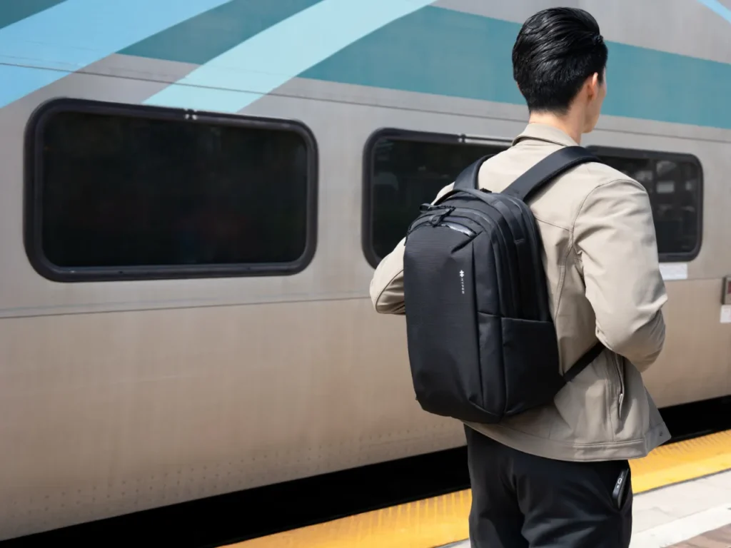 a man with a backpack standing next to a train. HyperPack Tech Backpack. {Tech} for Travel. https://techfortravel.co.uk