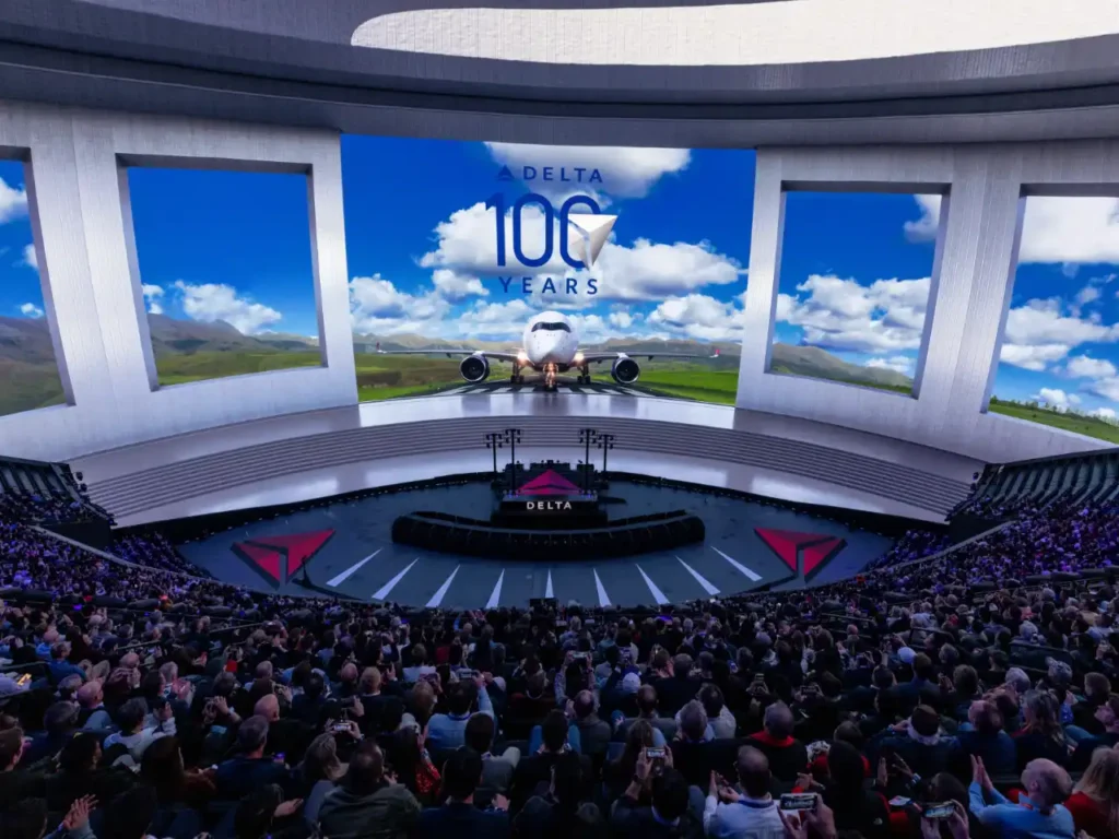Delta CES 2025 – {Tech} for Travel a large group of people in a large room with large screens. Delta App. {Tech} for Travel. https://techfortravel.co.uk