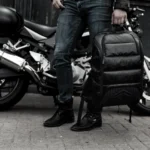 STM Goods Dux Backpack – {Tech} for Travel a person holding a backpack next to a motorcycle. Black Friday Deals 2025