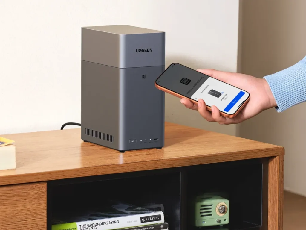 UGREEN Nasync DH2300 – {Tech} for Travel a person holding a phone next to a grey rectangular device. best travel gifts for Christmas 2025. {Tech} for Travel. https://techfortravel.co.uk