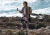 Hiking upgrade, the Ascentiz modular exoskeleton confirms 20 km range a woman standing on a rocky beach holding a camera. Ascentiz modular exoskeleton. CES 2026 News. {Tech} for Travel. https://techfortravel.co.uk