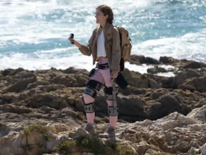 a woman standing on a rocky beach holding a camera. Ascentiz modular exoskeleton. CES 2026 News. {Tech} for Travel. https://techfortravel.co.uk