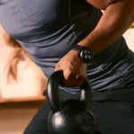 a person holding a kettlebell. Amazfit Active Max. {Tech} for Travel. https://techfortravel.co.uk