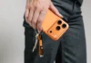 Nomad ChargeKey completes the look for Cosmic Orange iPhone owners a person holding a phone with keys. Nomad ChargeKey v2 Stellar Orange. {Tech} for Travel. https://techfortravel.co.uk