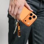 Nomad ChargeKey completes the look for Cosmic Orange iPhone owners a person holding a phone with keys. Nomad ChargeKey v2 Stellar Orange. {Tech} for Travel. https://techfortravel.co.uk
