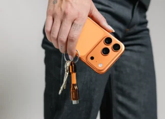 Nomad ChargeKey completes the look for Cosmic Orange iPhone owners a person holding a phone with keys. Nomad ChargeKey v2 Stellar Orange. {Tech} for Travel. https://techfortravel.co.uk