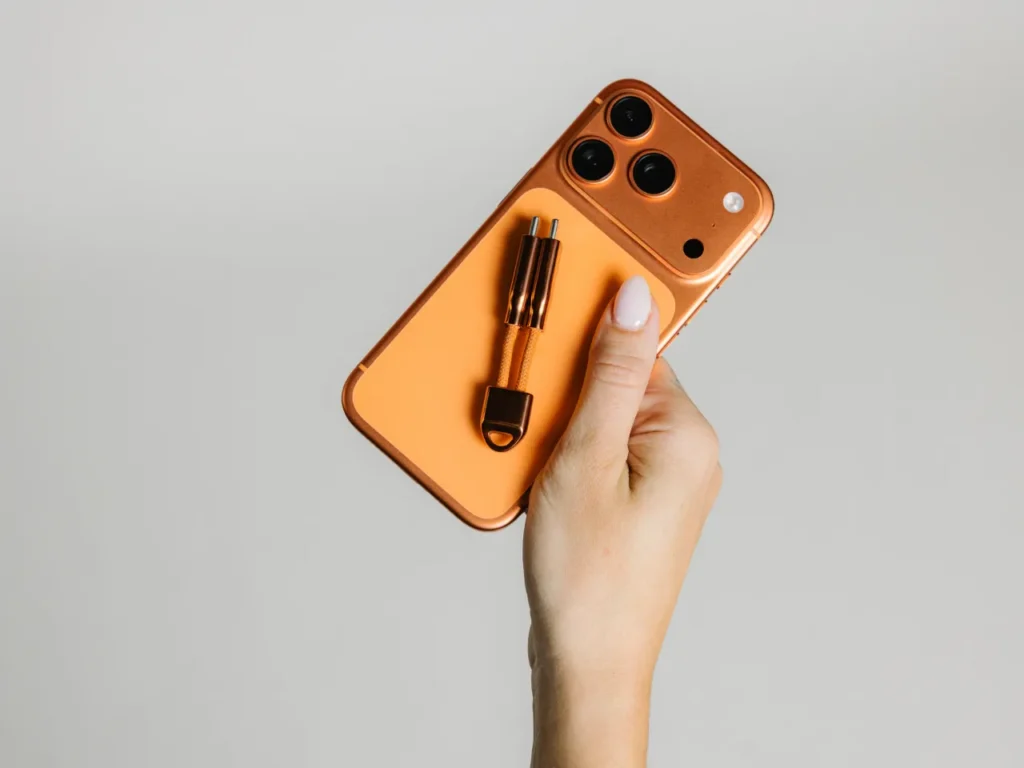 a hand holding a phone. Nomad ChargeKey V2 Stellar Orange. {Tech} for Travel. https://techfortravel.co.uk