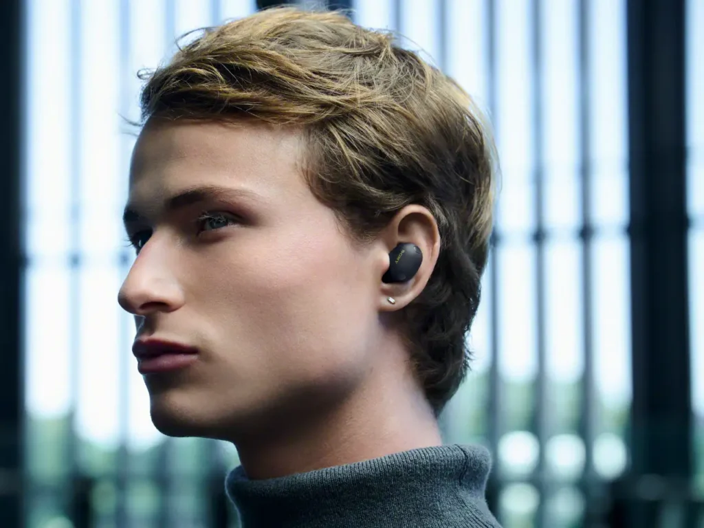 a man with earbuds in his ear. Sony WF-1000XM6 Earbuds. {Tech} for Travel. https://techfortravel.co.uk